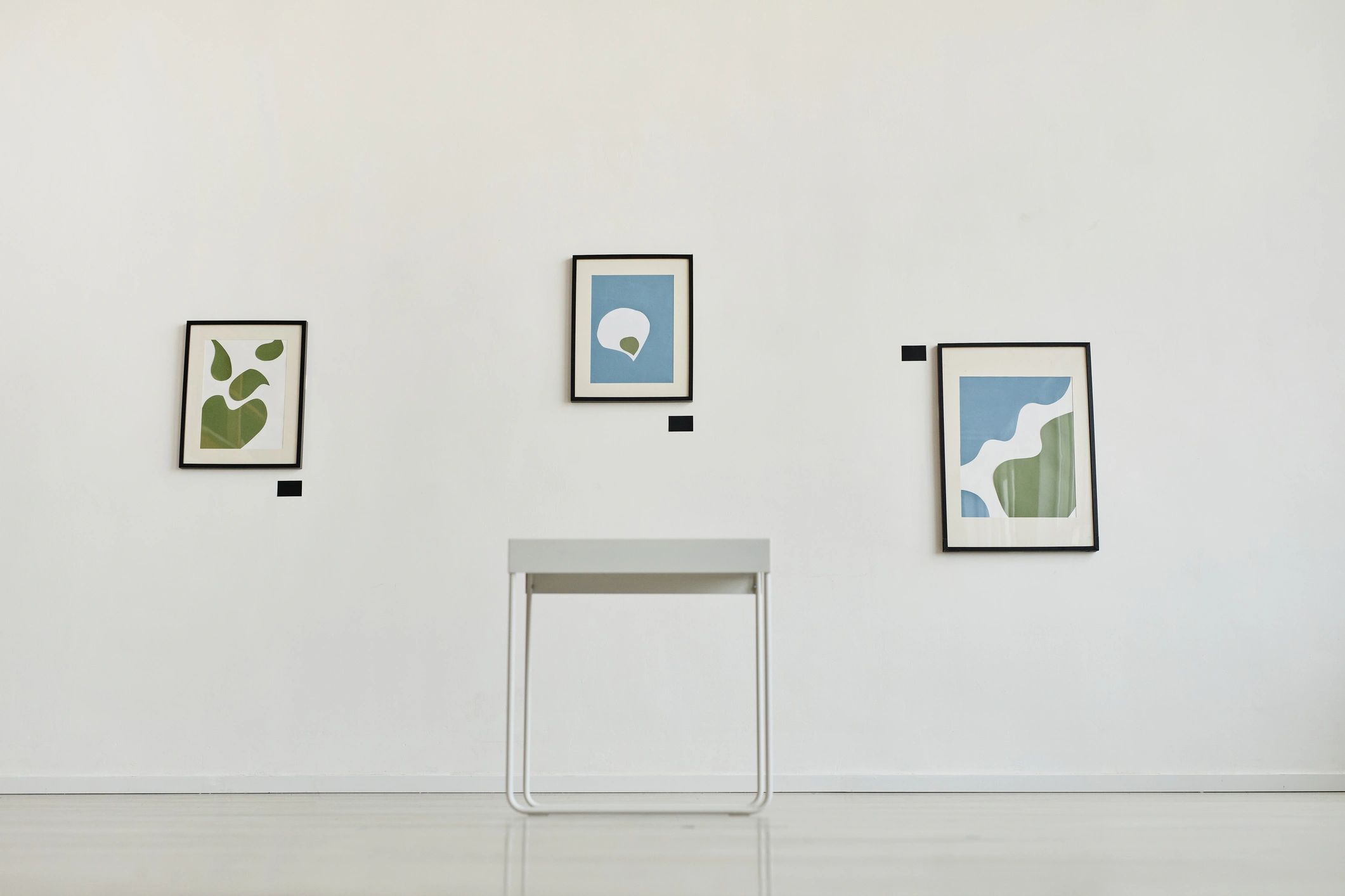 Beyaz duvarda sergilenen modern tabloların bulunduğu minimal galeri alanı